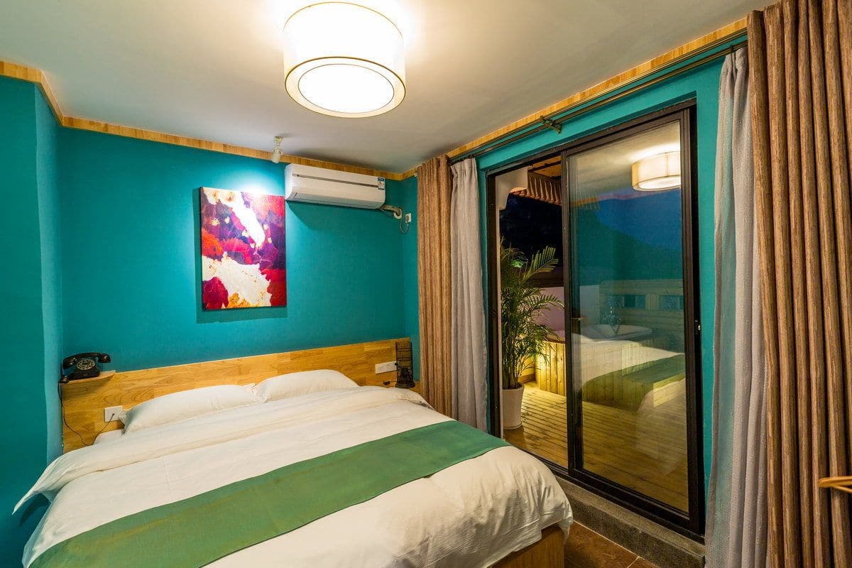 A hotel room with a bed, a painting on the wall, an air conditioning unit, and a sliding glass door leading to an outdoor area.