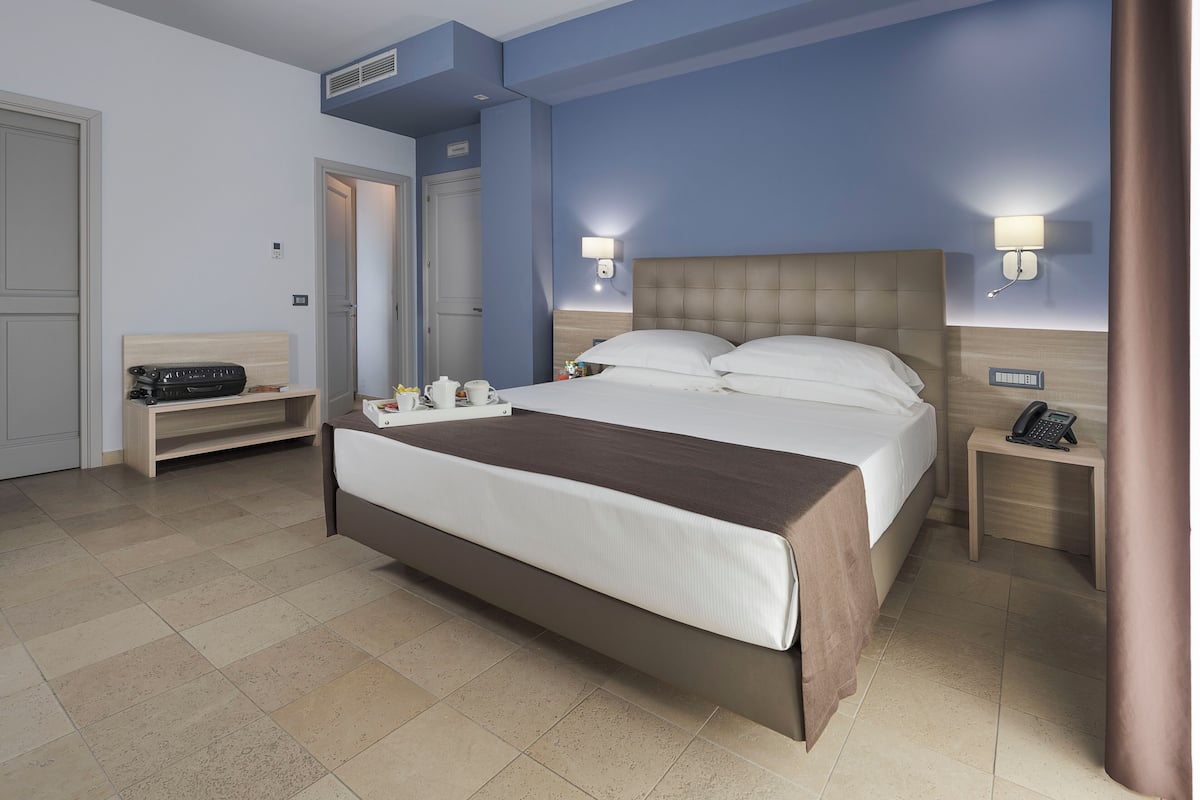 A hotel room with a large bed, bedside tables, a mirror, and a wall-mounted phone.
