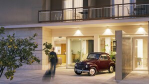 Fachada de un edificio con un automóvil clásico estacionado, un balcón con barandilla y un mostrador de recepción.