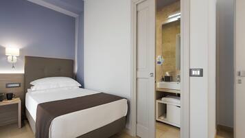 Une chambre d’hôtel avec un lit, une table de chevet, une lampe et une salle de bain visible à travers une porte ouverte.