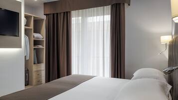A hotel room with a bed, a TV mounted on the wall, a wardrobe, and a window with curtains.
