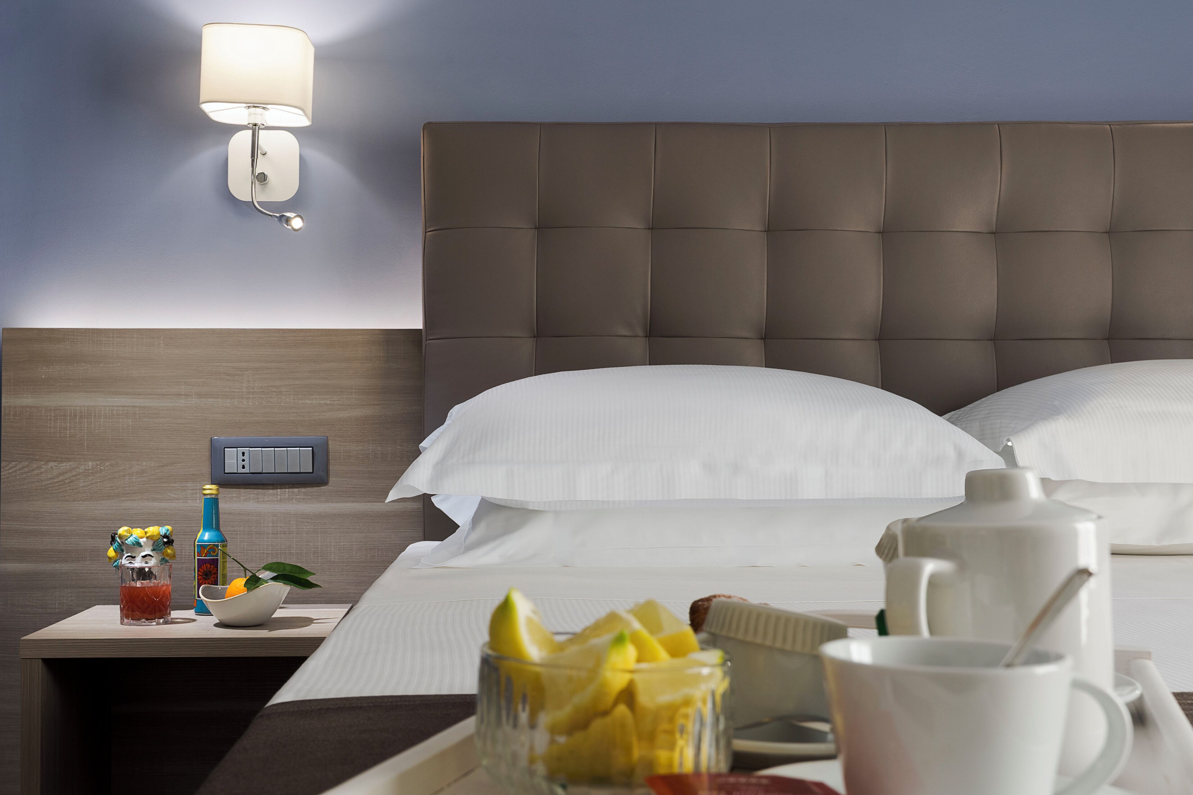 Een hotelkamer met een bed, nachtkastje, lamp en ontbijtartikelen.