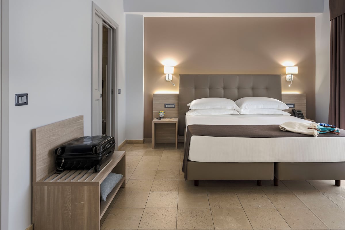 A hotel room with a bed, bedside tables, a lamp, a suitcase, and a bench.