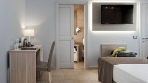 Habitación de hotel con cama, escritorio con silla, televisor montado en la pared y baño visible a través de una puerta abierta.