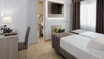 A hotel room with a bed, a desk, a chair, a TV mounted on the wall, and a bathroom visible through an open door.