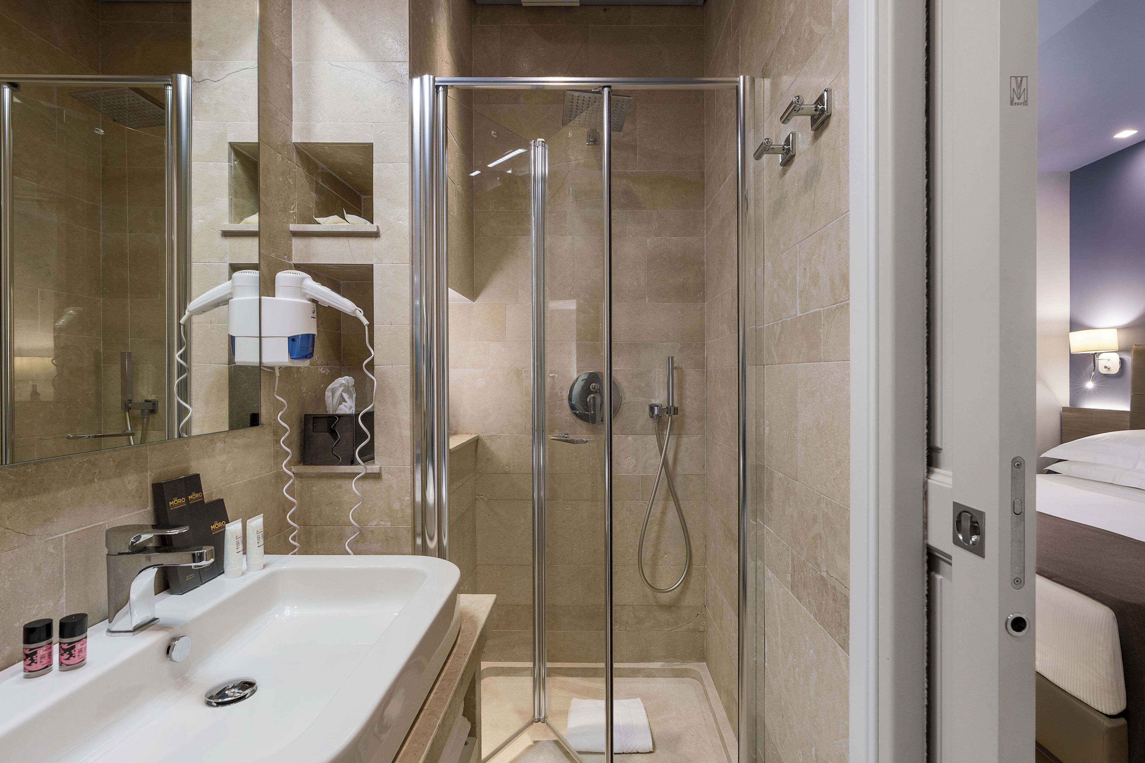 Een moderne badkamer met een douchecabine van glas, een witte wastafel met toiletartikelen en een spiegel.