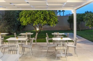 Un patio al aire libre con mesas y sillas, un árbol y una vista de un edificio al fondo.