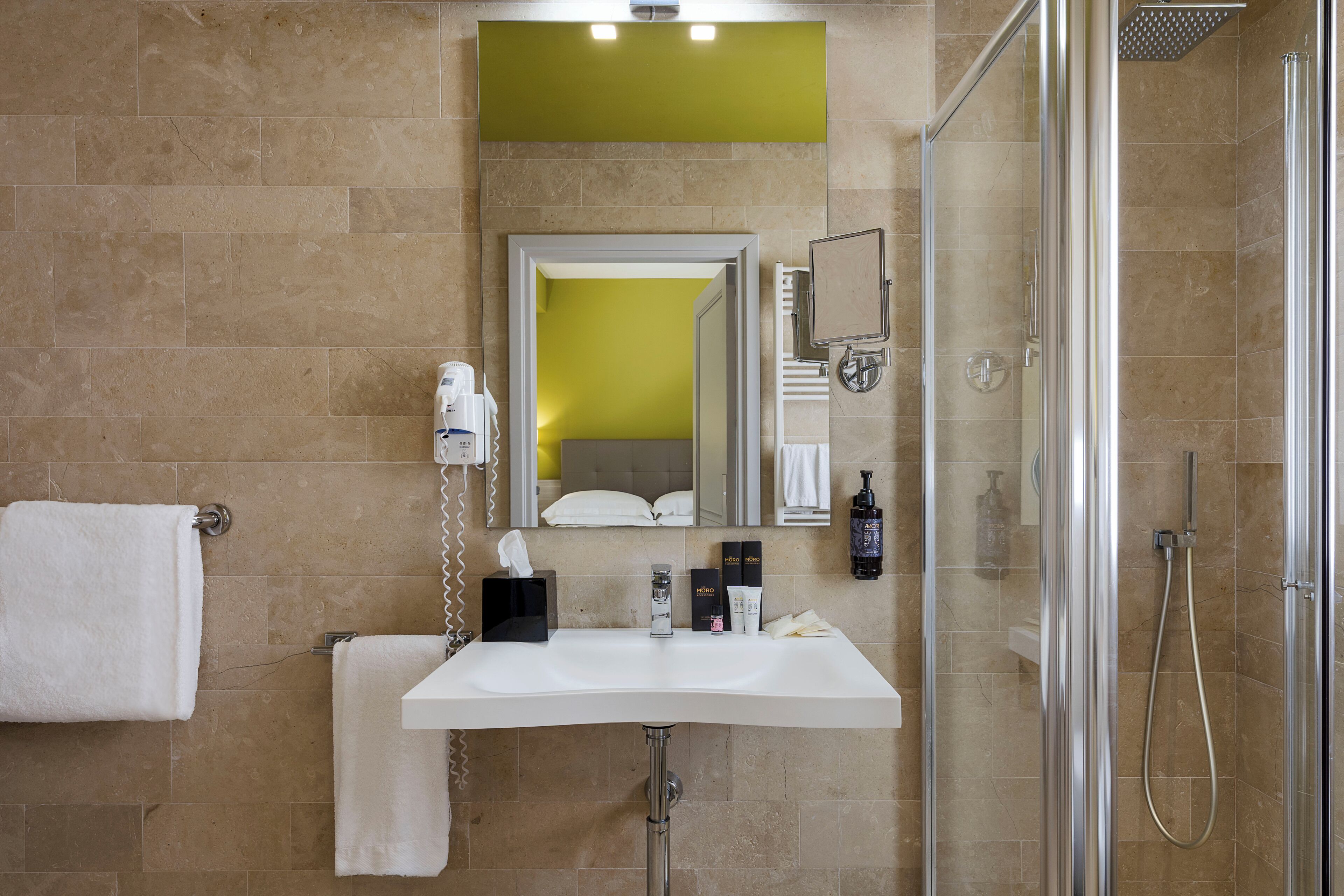 Une salle de bain avec un lavabo blanc, un miroir, un porte-serviettes, une douche en verre et un mur d’accent vert.