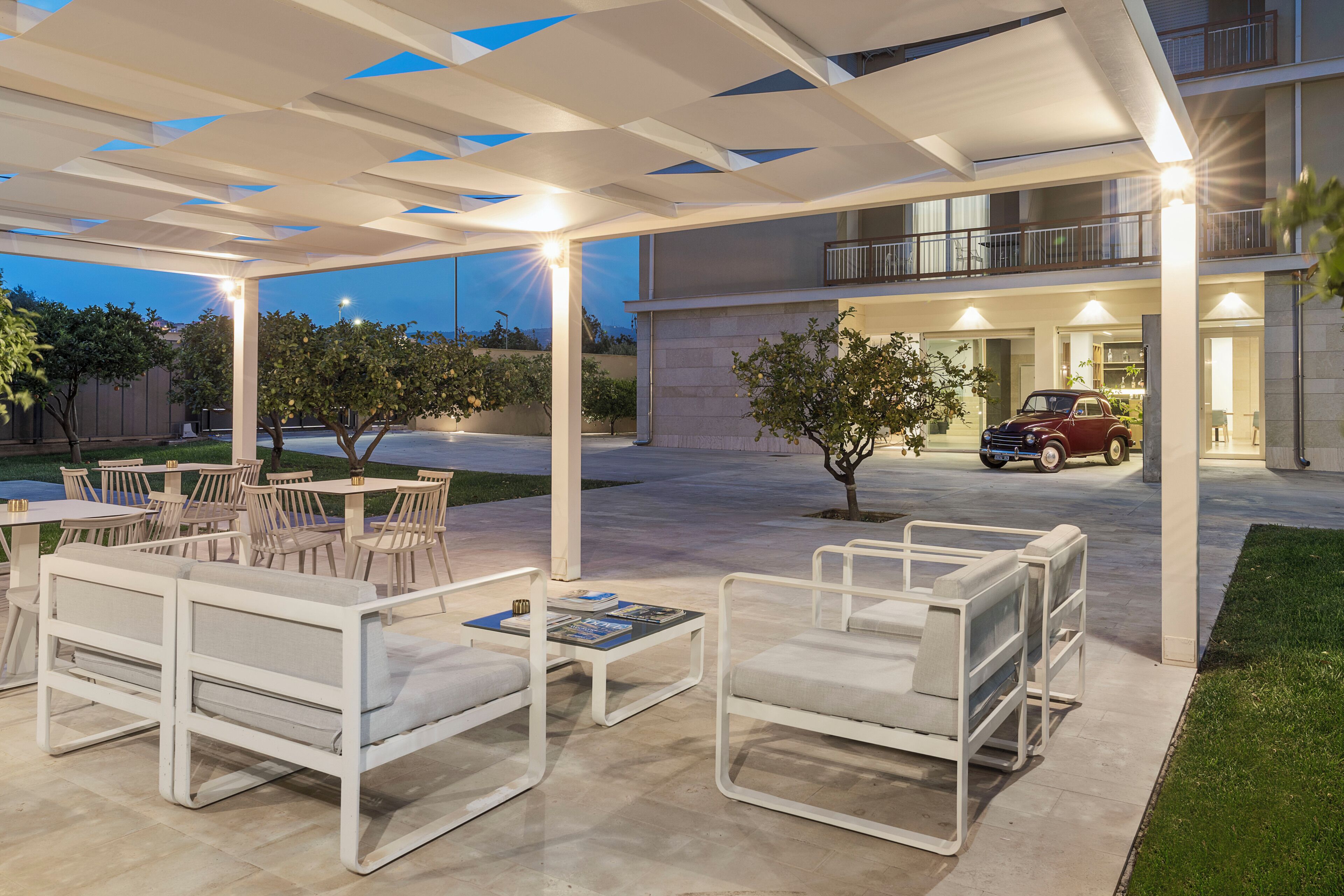 An outdoor seating area with white furniture, a covered patio, and a building with a balcony.