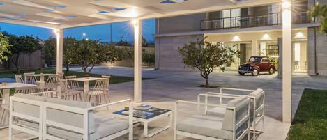 An outdoor seating area with white furniture, a covered patio, and a building with a balcony.