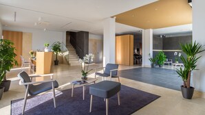 Un vestíbulo amplio con mostrador de recepción, zona de estar, escalera y plantas en macetas.