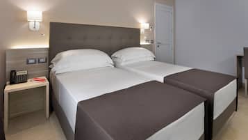 Ett hotellrum med två sängar, ett nattduksbord med en telefon och en väggmonterad lampa.