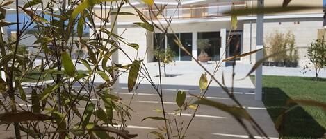 A modern building with a glass facade, a concrete ground floor, and a small green area with plants.