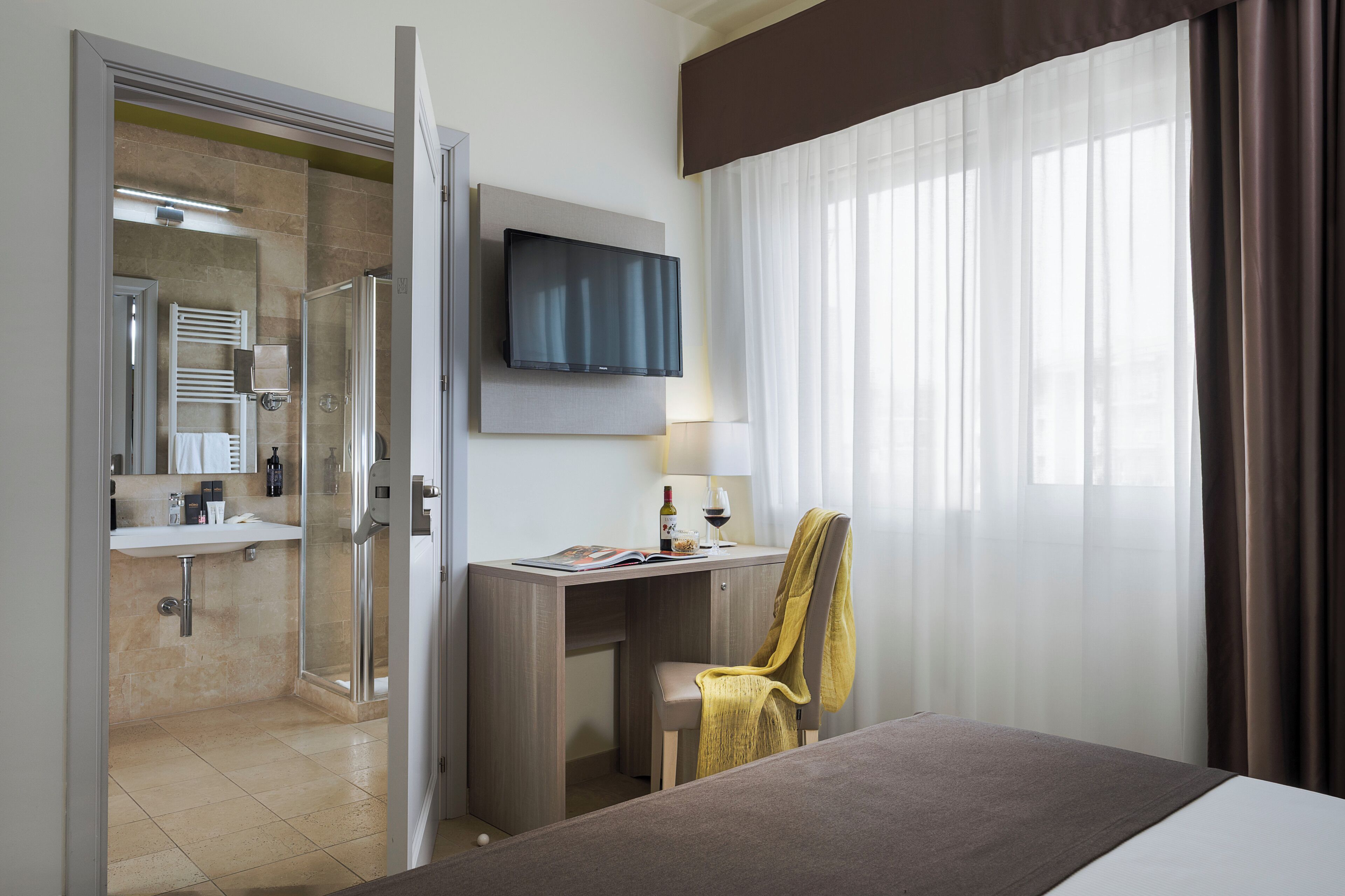 A hotel room with a bed, a desk, a TV, a shower, and a bathroom.