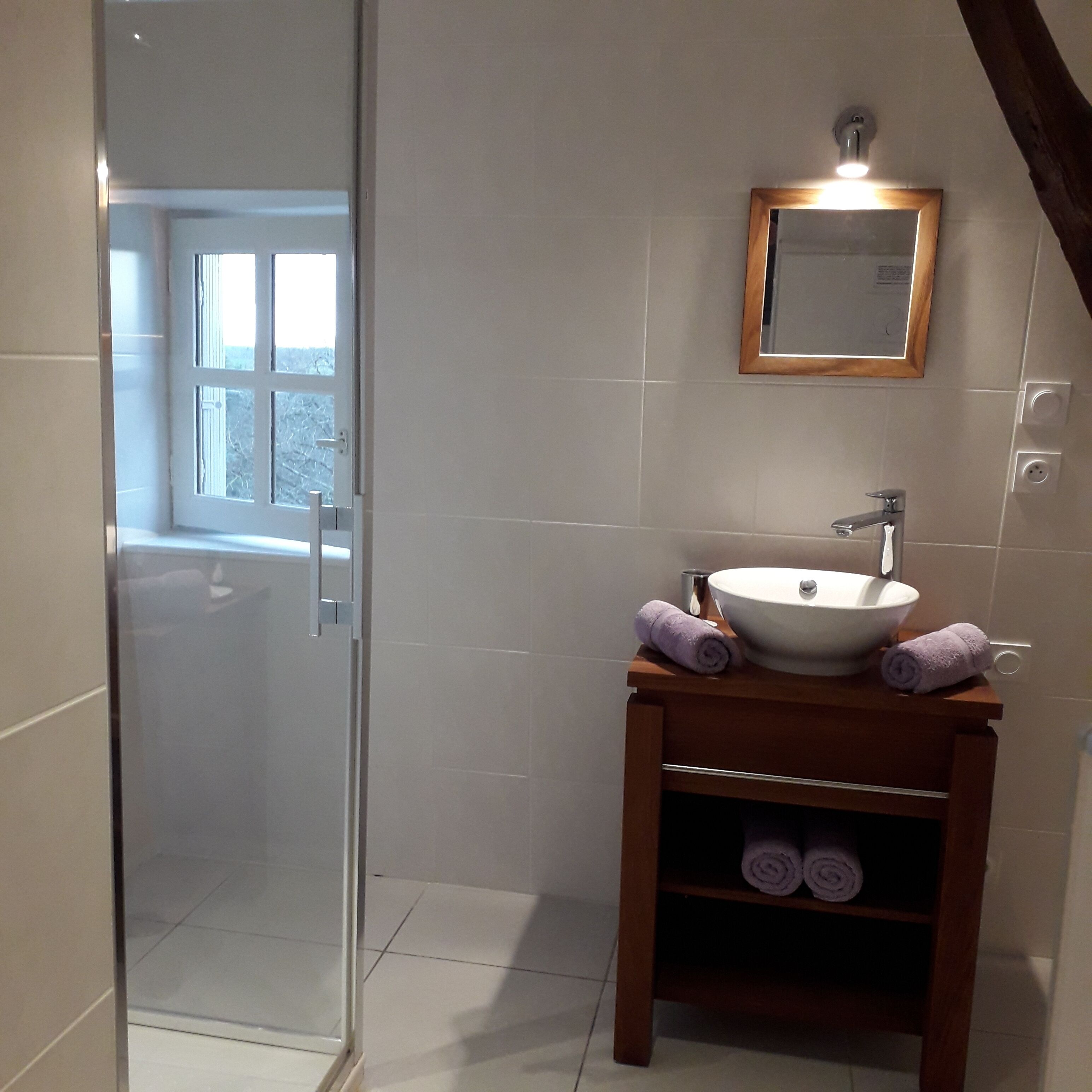 Un baño con mampara de vidrio, lavamanos blanco y tocador de madera.