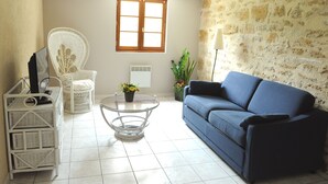 Ein Wohnzimmer mit einem blauen Sofa, einem weißen Korbstuhl, einem Glastisch und einem weißen Schrank.