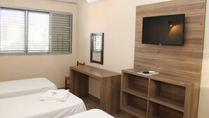 A hotel room with two beds, a TV mounted on a wooden wall, a desk, and a window with blinds. - Espigão Palace Hotel (Resende)