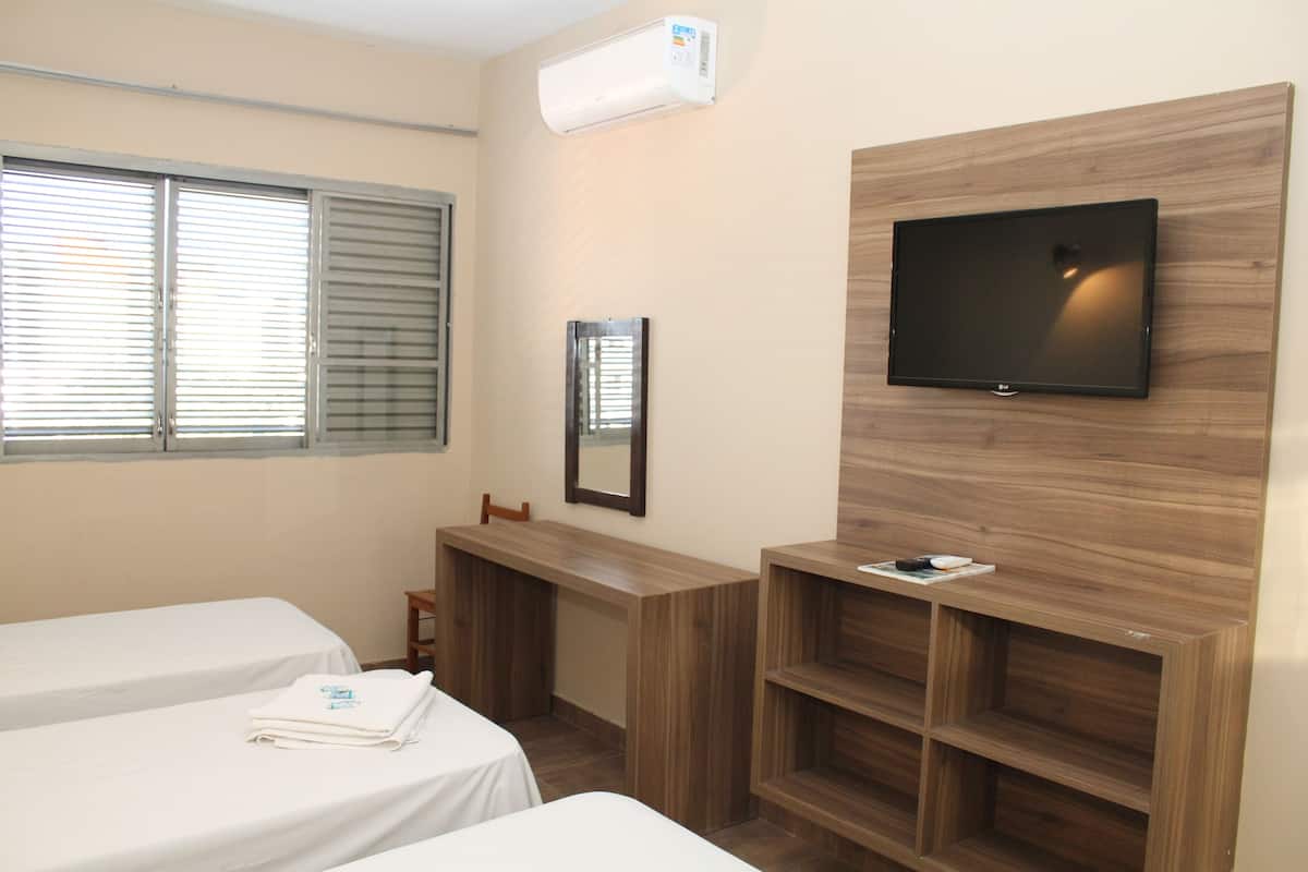 Habitación de hotel con dos camas, un televisor montado en una pared de madera, un escritorio y una ventana con persianas.