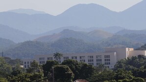 A building with a flat roof and rectangular windows, surrounded by lush greenery and mountains in the background. - Espigão Palace Hotel (Resende)