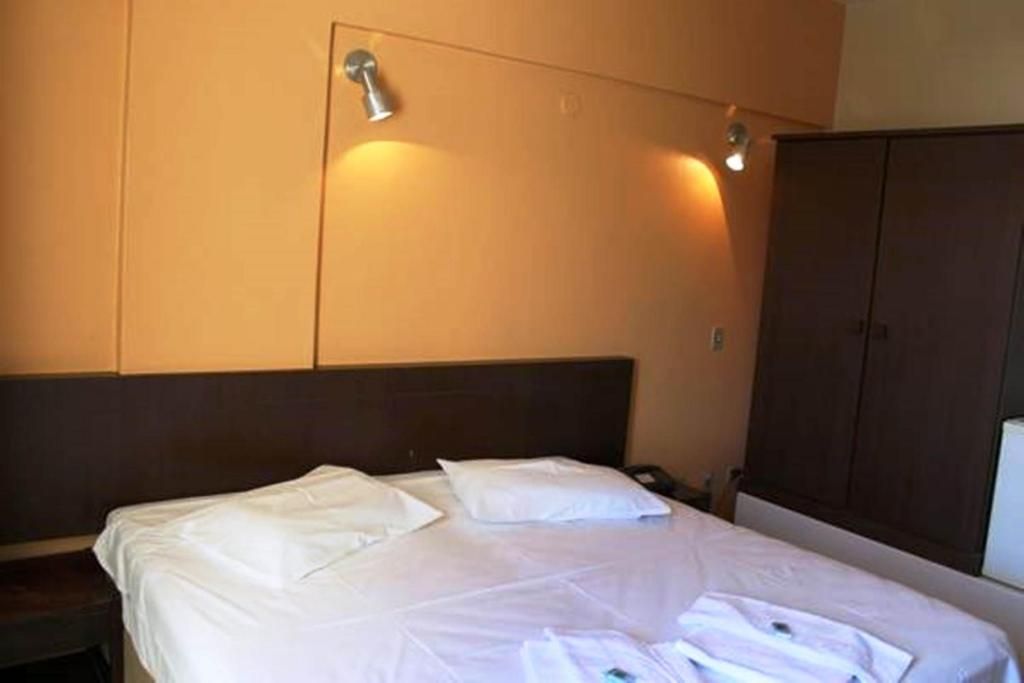 Una habitación de hotel con una cama, un armario y una lámpara de pared.