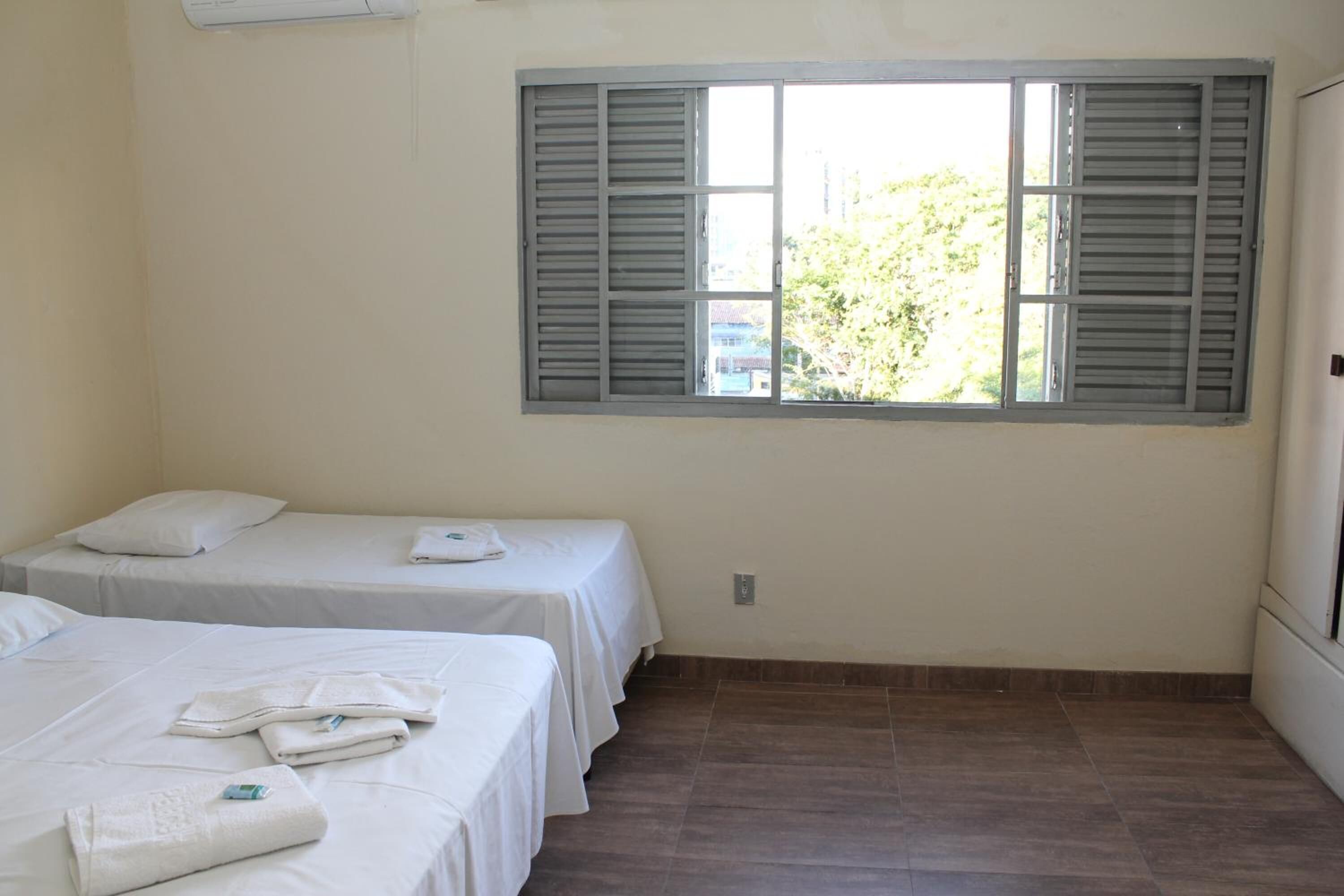 A room with two single beds, a window with shutters, and a tiled floor.