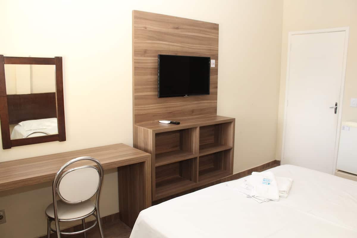 Habitación de hotel con cama, televisión montada en un panel de madera, escritorio con silla y armario.