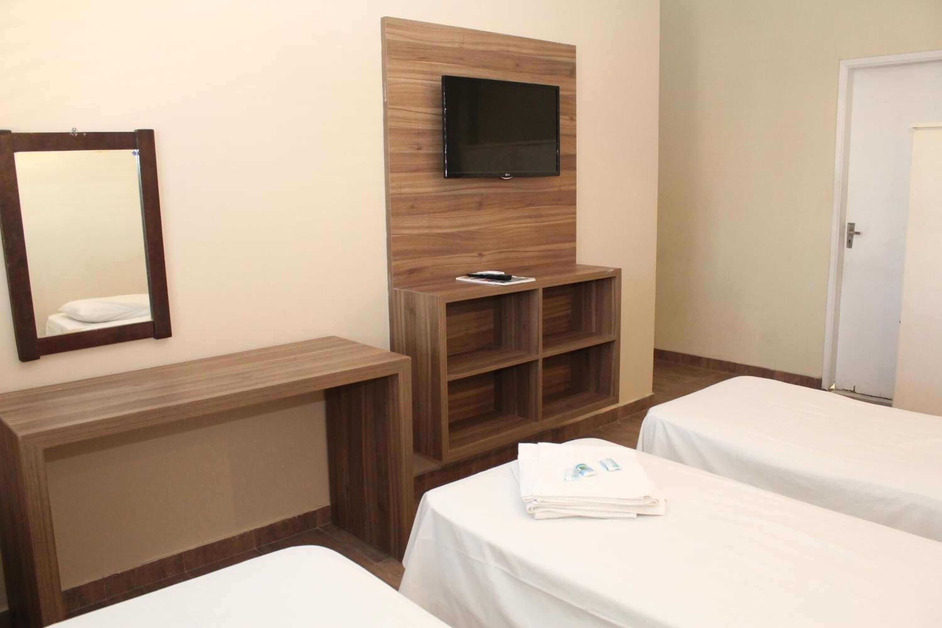 A hotel room with a wooden console table, a TV mounted on the wall, a mirror, two beds with white linens, and a door.