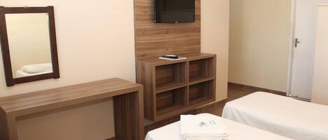 A hotel room with a wooden console table, a TV mounted on the wall, a mirror, two beds with white linens, and a door.