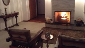 A cozy living room with a fireplace, a wooden chair, a small table, and a mirror on the wall. - Hotel La Ponsa Itatiaia (Itatiaia)