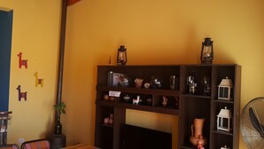 Una cocina compacta con armarios blancos, un comedor con mesa y sillas, y una sala de estar con una estantería y elementos decorativos.