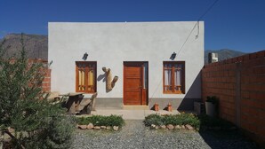 Un edificio de fachada sencilla, con dos ventanas de madera, una puerta central y un pequeño jardín con rocas y plantas.