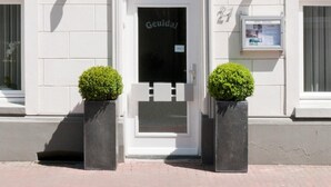 A building with a white facade, blue shutters, a decorative crest above the entrance, and a sign reading "Geulad".
