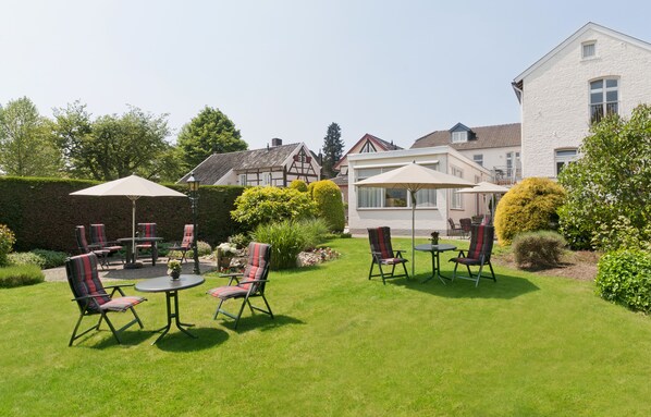 A well-maintained garden with a patio area featuring outdoor furniture and umbrellas. - Appartementen-Hotel Geuldal (Epen)