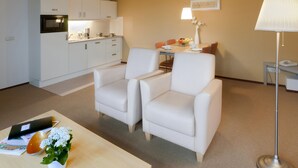 A modern kitchen with white cabinets and a microwave, a dining area with a table and chairs, and a floor lamp.