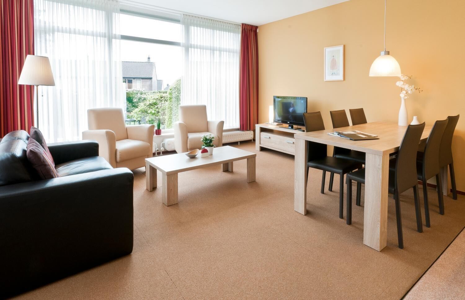 A modern living room with a sofa, chairs, a coffee table, a TV, and a dining area with chairs and a table.
