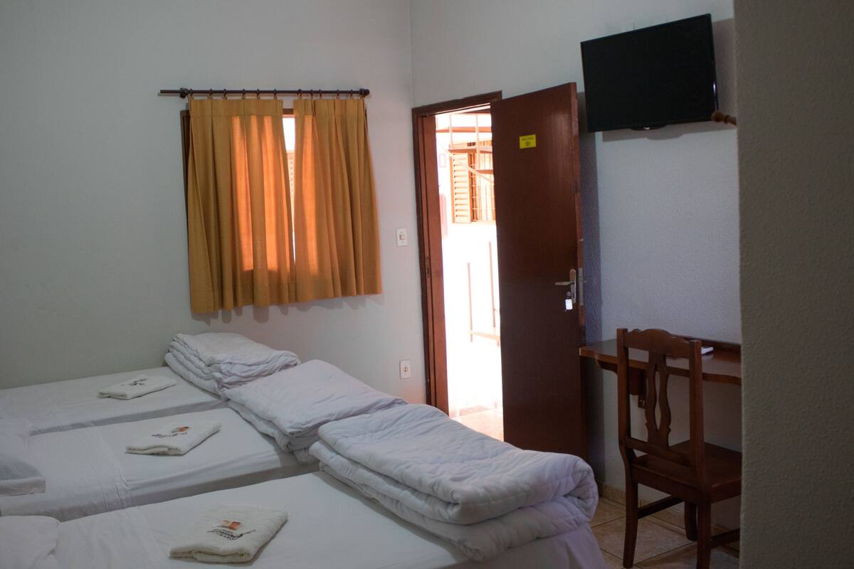 A room with two beds, a chair, a television, and a door leading to another room.