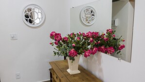 A bathroom with a wooden bench, a white vase with pink flowers, and a mirror with a circular window design. - Hotel Jeremias (Barretos)