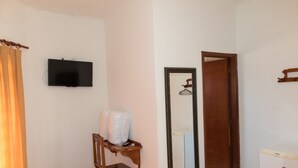 A room with a television mounted on the wall, a wooden chair with a tray, a mirror, and a door. - Hotel Jeremias (Barretos)
