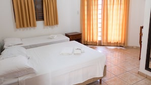 A hotel room with two beds, a wooden nightstand, a small table, and a window with curtains. - Hotel Jeremias (Barretos)