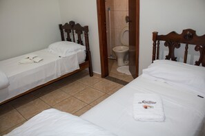 A hotel room with two single beds, a wooden headboard, a bathroom with a toilet and a shower area. - Hotel Jeremias (Barretos)