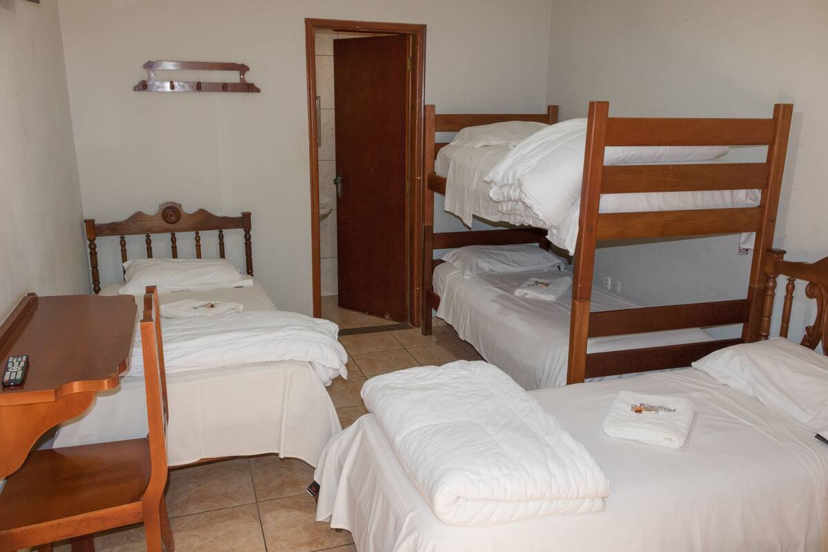 A room with bunk beds, a wooden desk, and a chair. There is a door leading to another room.