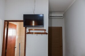 A room with a television mounted on the wall, an air conditioning unit, a wooden door, and a tiled floor. - Hotel Jeremias (Barretos)