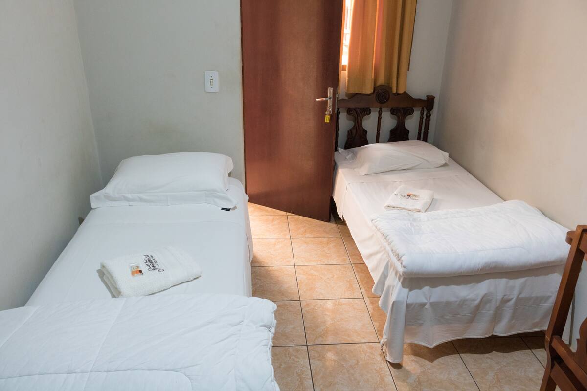 A small, clean room with two single beds, a wooden headboard, and a door leading to another room.
