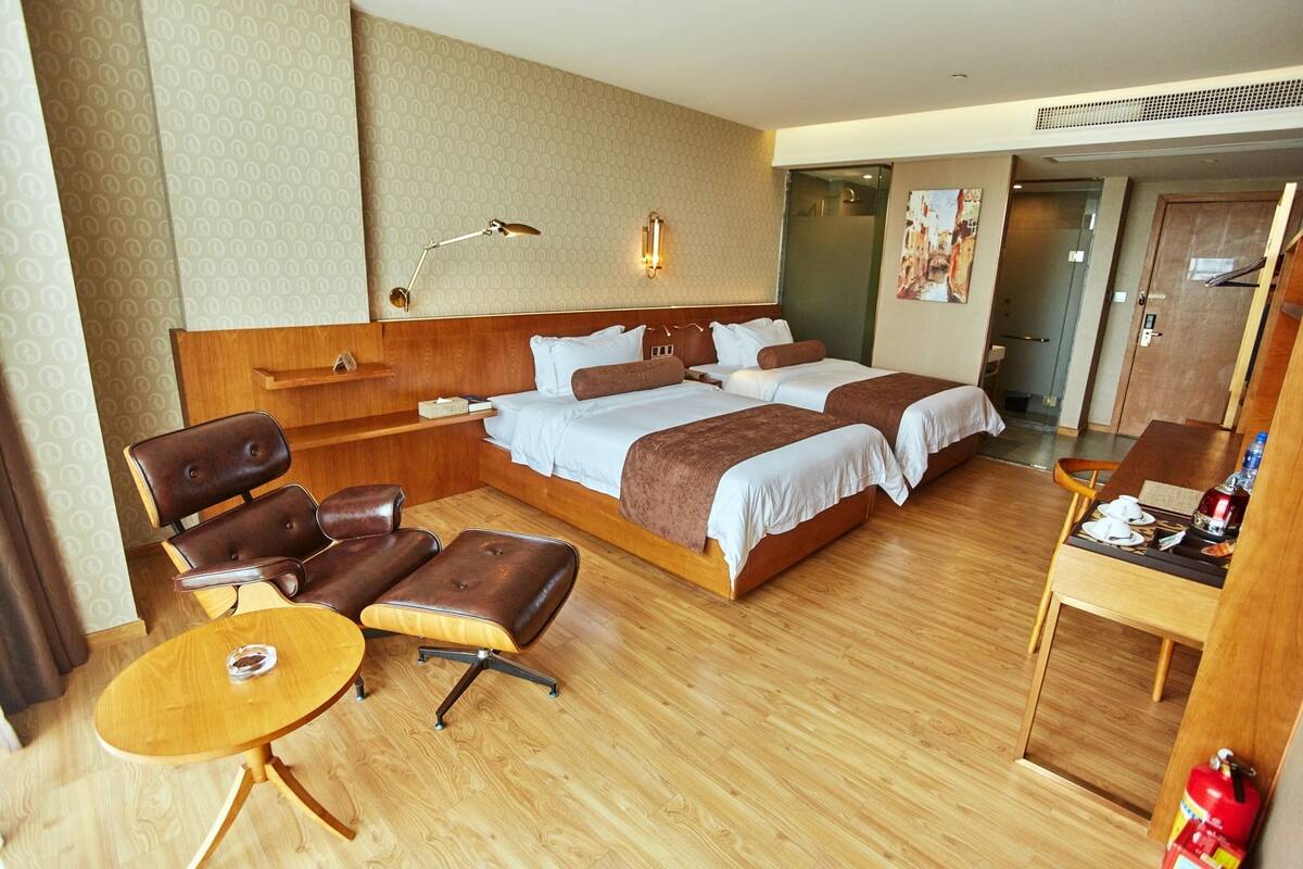 A hotel room with a large bed, two bedside tables, a desk with a chair, a small round table, and a sofa.