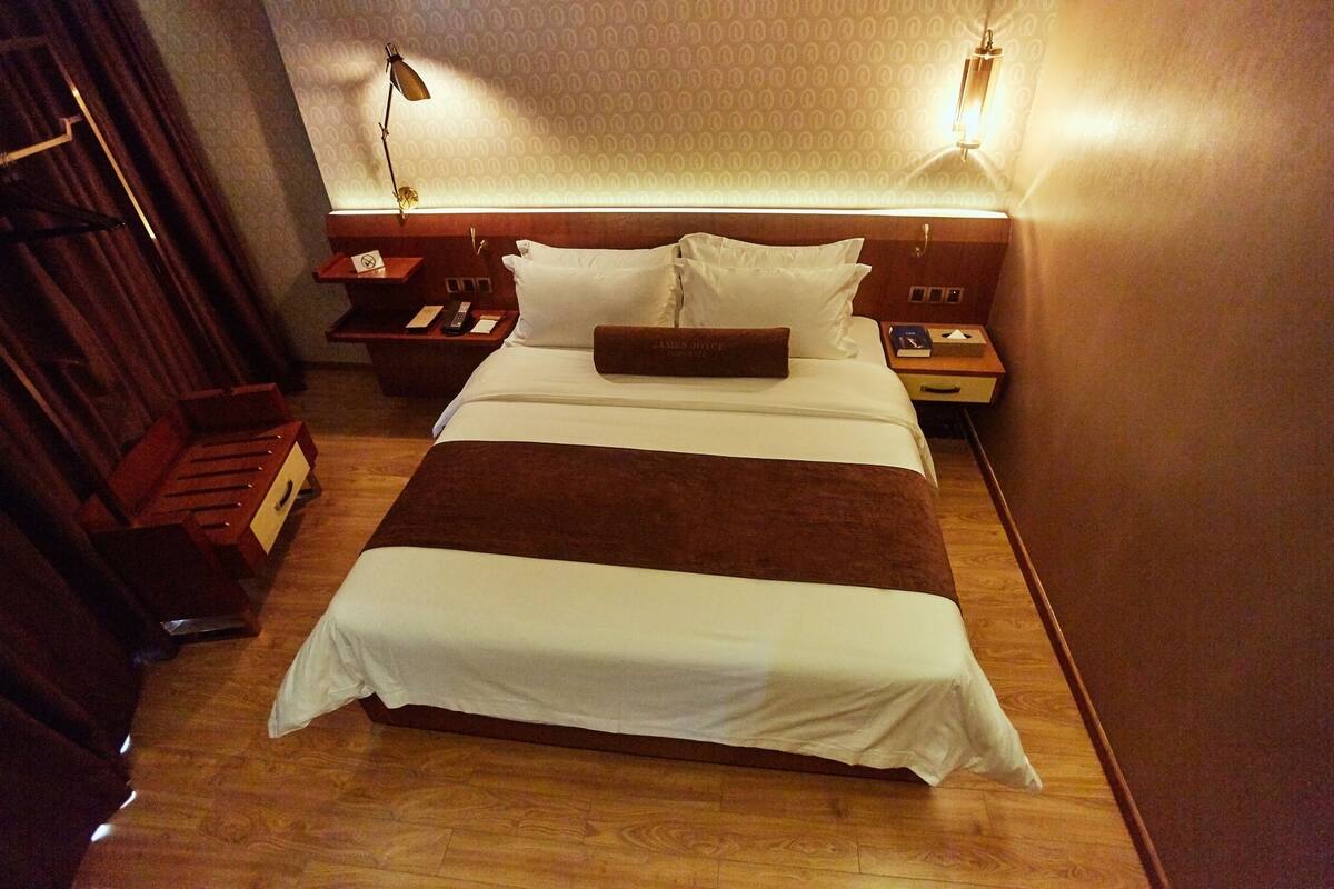 A hotel room with a large bed, wooden headboard, bedside tables, and a nightstand.