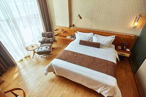 Quarto de hotel com uma cama grande, uma escrivaninha, uma cadeira, uma mesa pequena e um abajur.