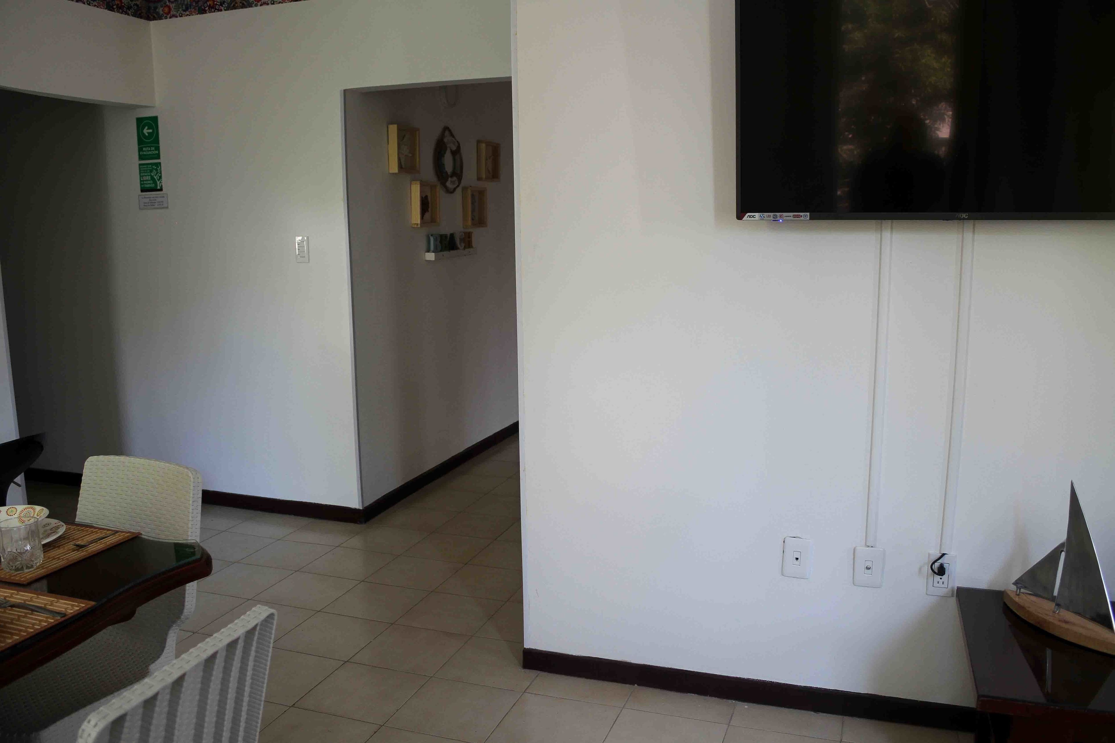 A hotel room with a dining area, a TV mounted on the wall, and a small table with a chair.