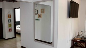 A room with a bed, a mirror, a television, and a small table with a lamp.
