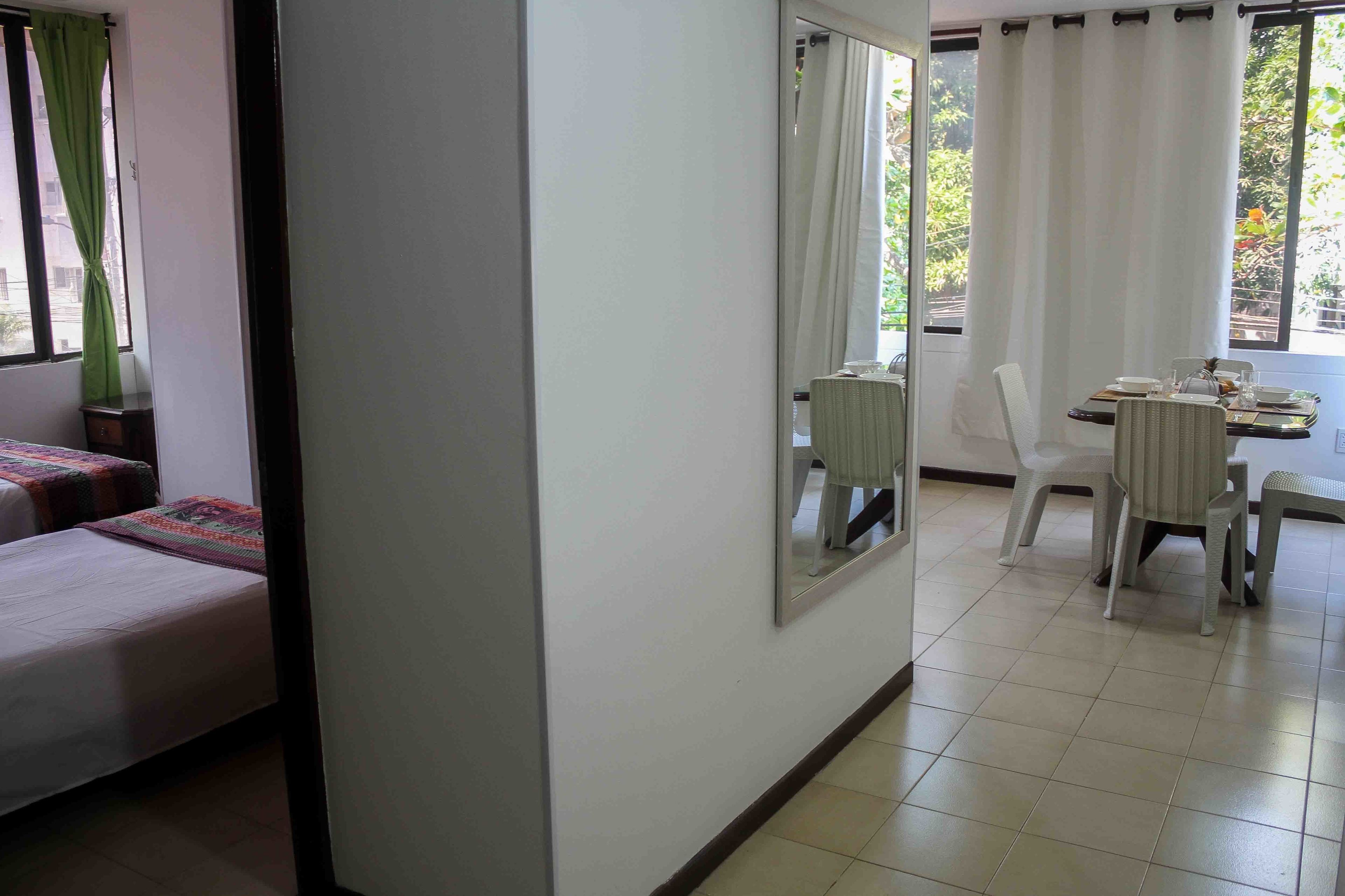 A hotel room with a bed, a dining table with chairs, a mirror, and a view of the outside.