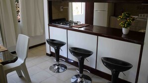 A kitchen with a gas stove, three black bar stools, a white chair, and a potted plant.